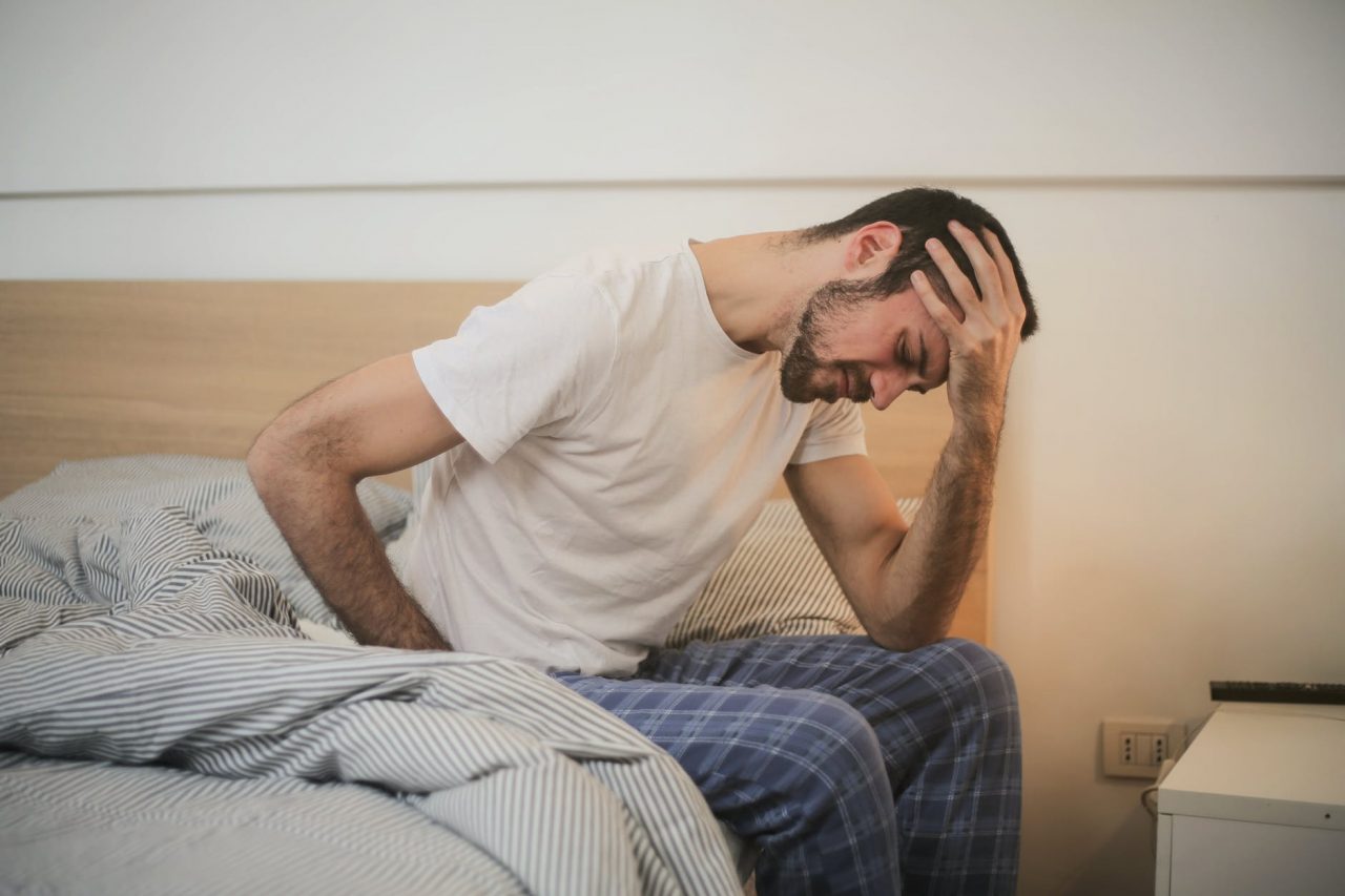 Tired man sitting on the edge of his bed.