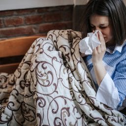 Woman with stuffy nose from allergies sitting on a couch.