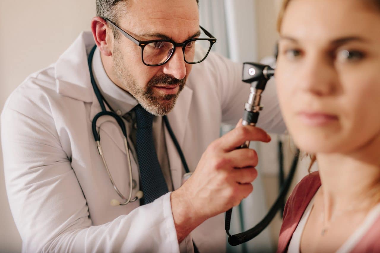 ENT doctor checking ear with otoscope of woman patient at hospital. Physician examining ear of female patient with an instrument.