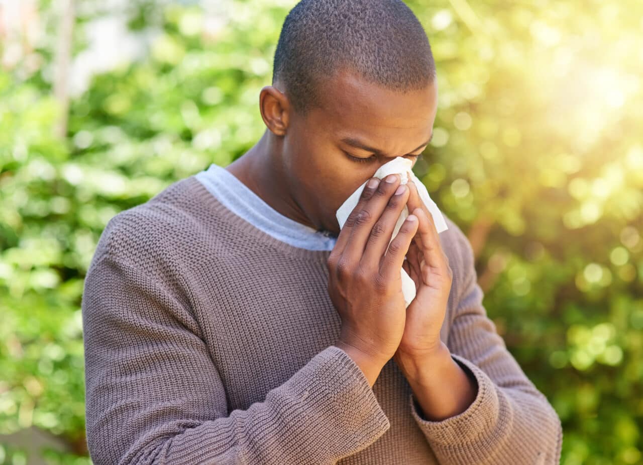 Shot of a young man blowing his nose outdoors