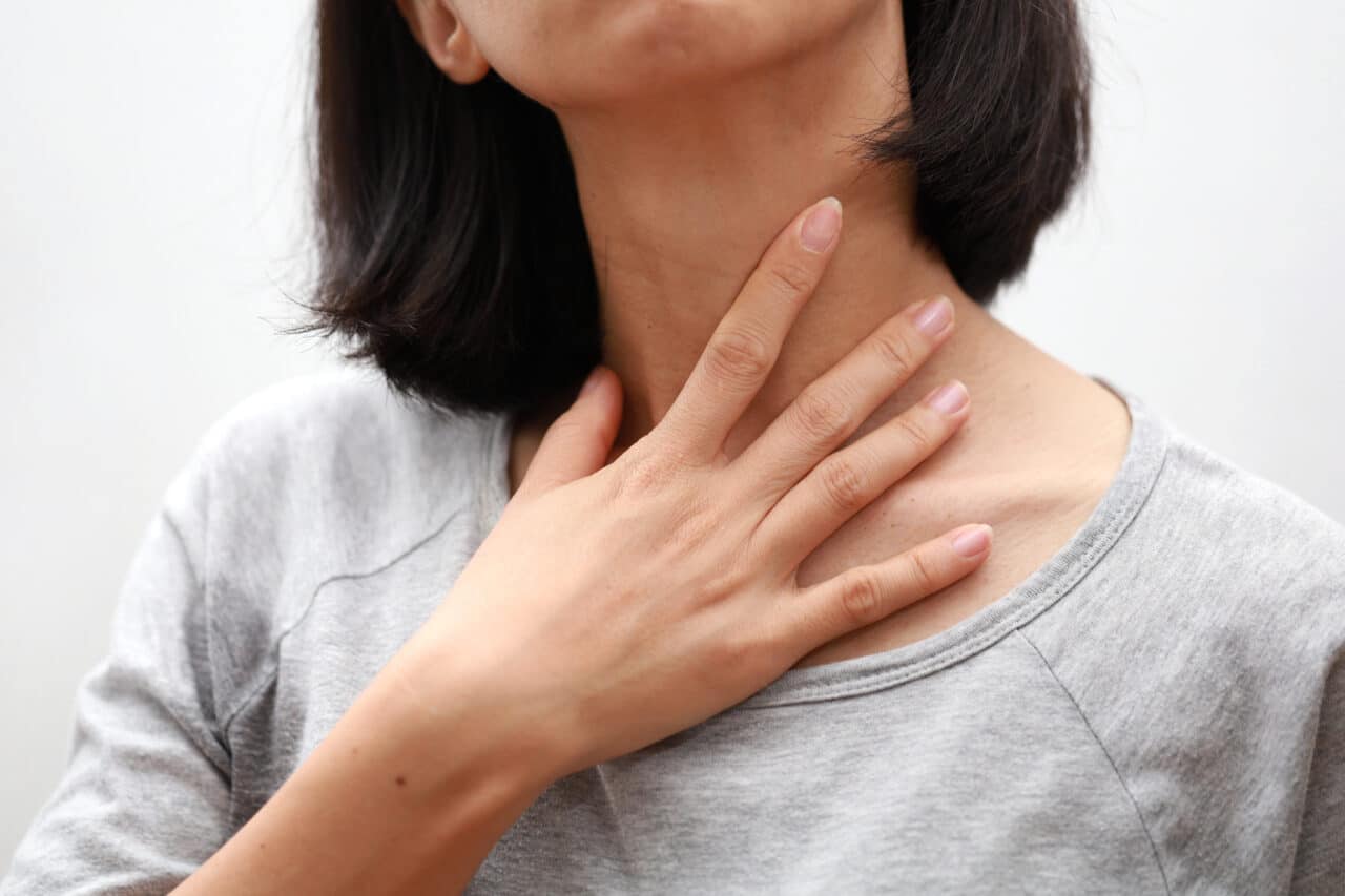 A woman with a sore throat touching her neck.