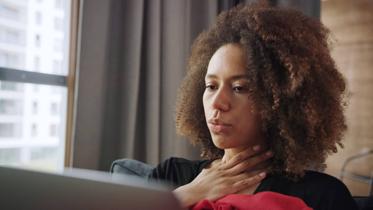 Sick woman putting a hand to her sore throat.