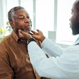 Doctor performing a throat exam on an older man.
