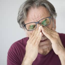 Older man with glasses rubbing his eyes.