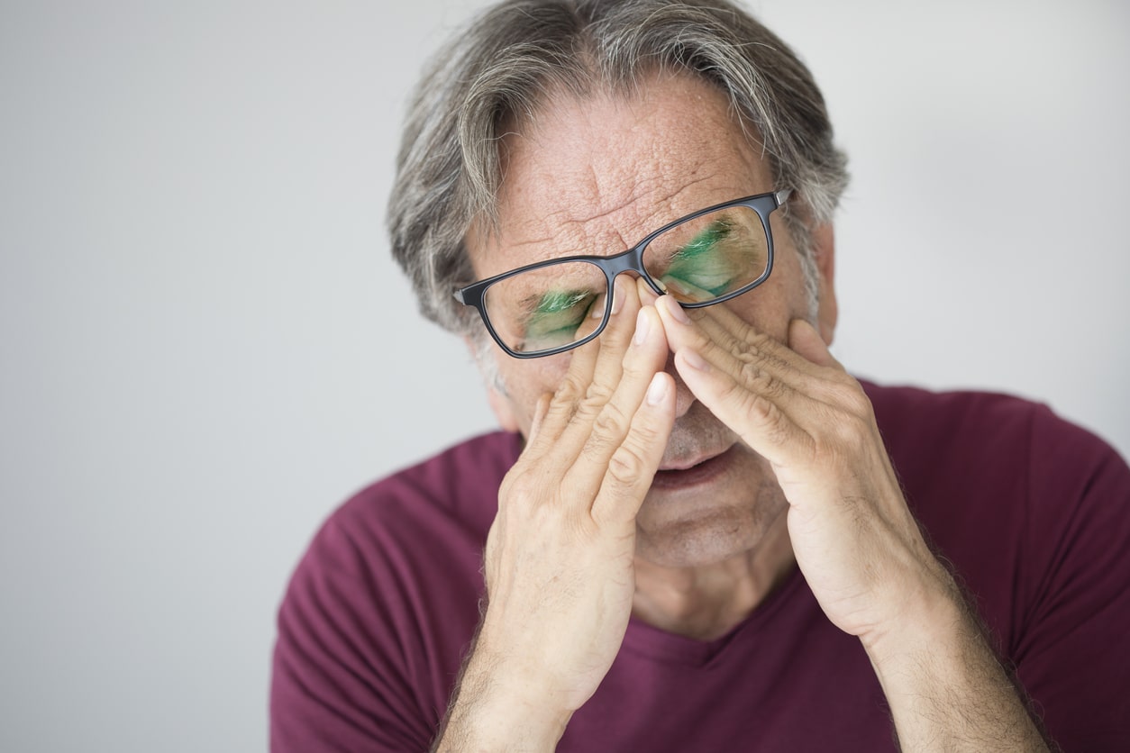 Older man with glasses rubbing his eyes.