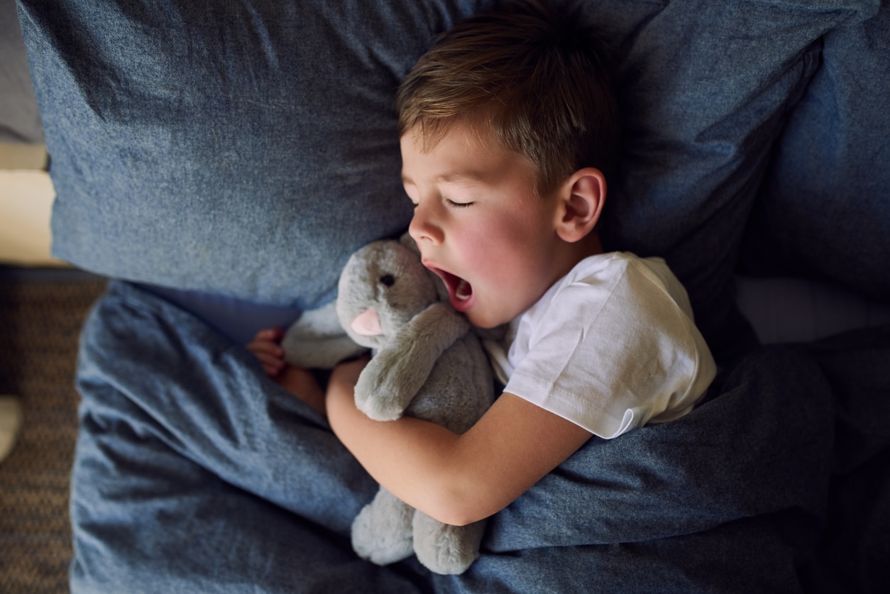 Young boy yawns in bed